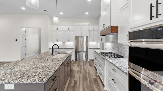 kitchen with sink, a kitchen island with sink, white cabinetry, and stainless steel appliances