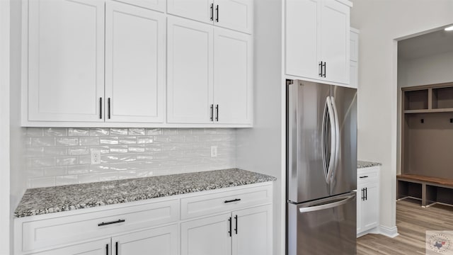 kitchen featuring white cabinets, light hardwood / wood-style flooring, stone counters, and stainless steel refrigerator