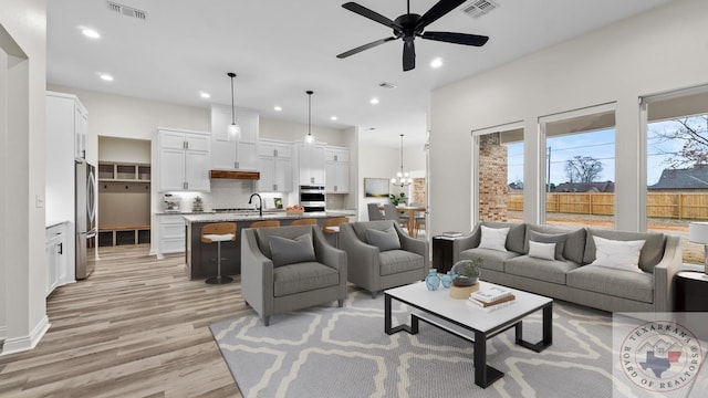 living room featuring sink, ceiling fan with notable chandelier, and light hardwood / wood-style floors