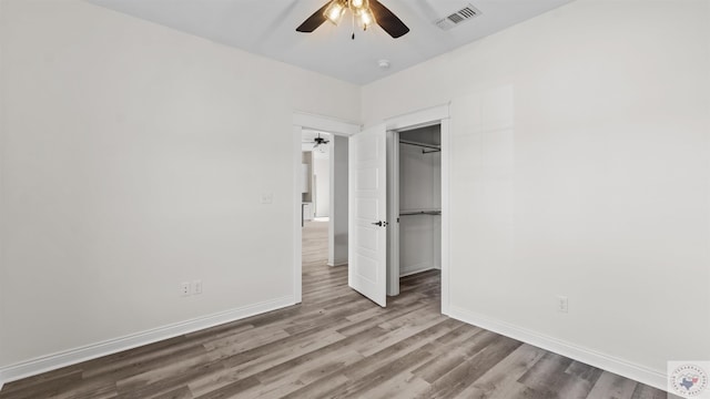 unfurnished bedroom with a walk in closet, ceiling fan, a closet, and wood-type flooring