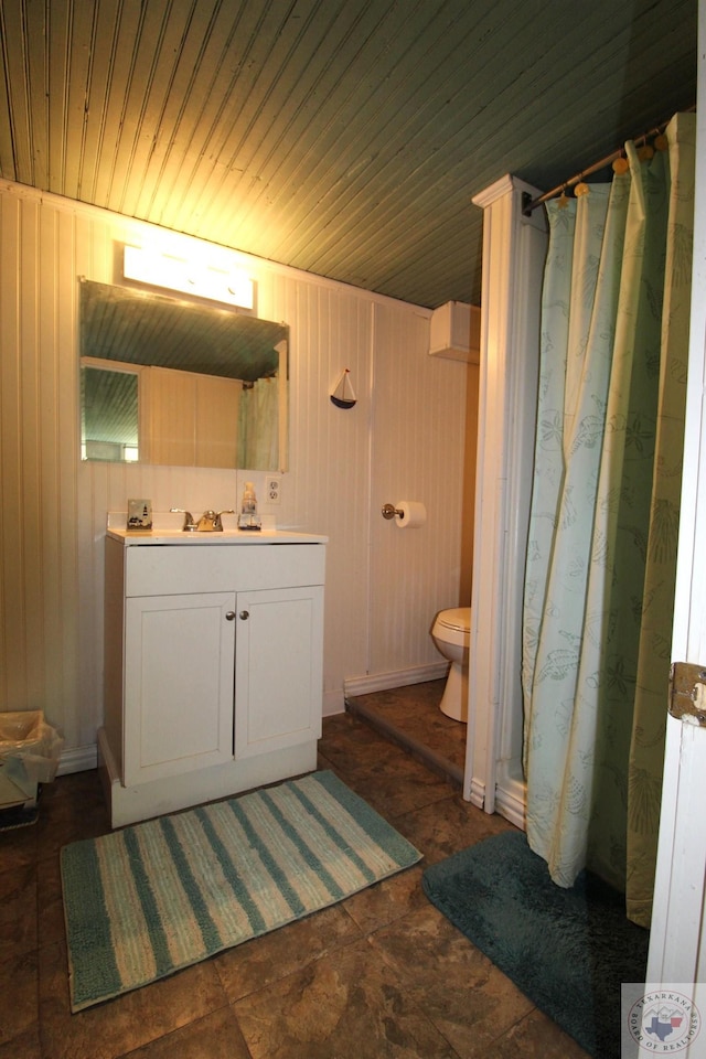 bathroom with vanity, toilet, wood walls, and a shower with curtain