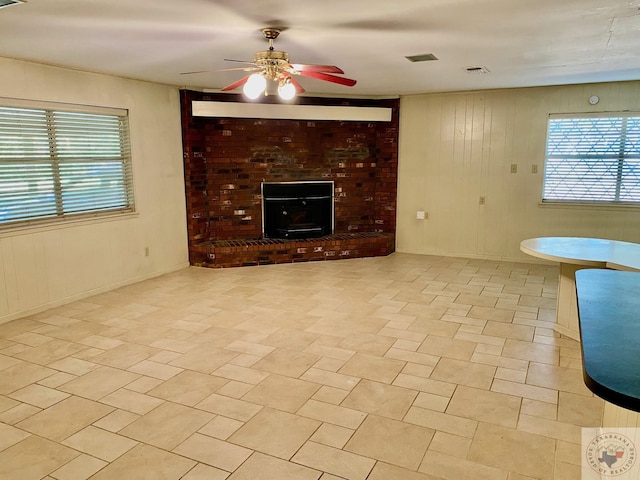 unfurnished living room with ceiling fan, a brick fireplace, and wood walls