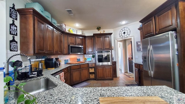 kitchen featuring stainless steel appliances, dark brown cabinetry, light stone counters, decorative backsplash, and sink