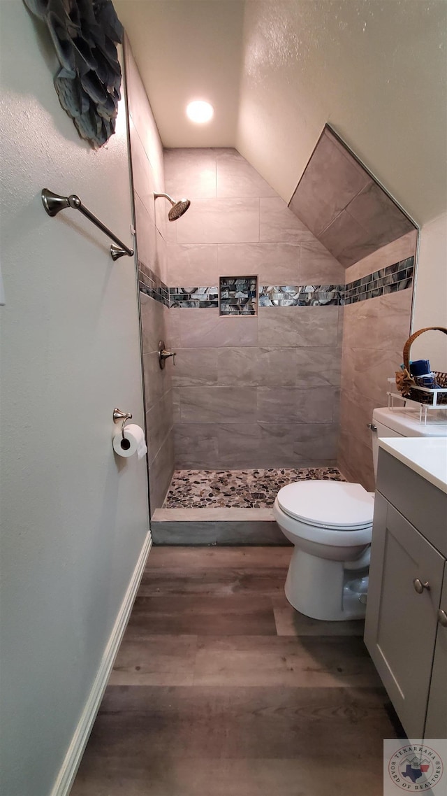 bathroom featuring hardwood / wood-style flooring, toilet, vaulted ceiling, vanity, and tiled shower