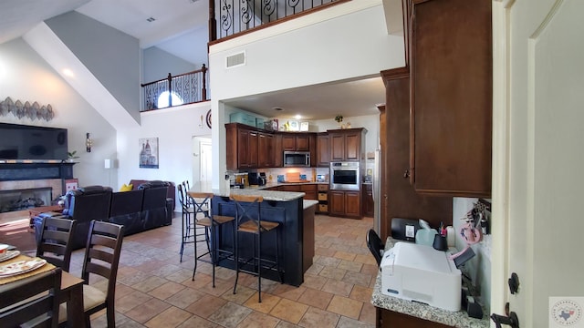 kitchen with a towering ceiling, light stone countertops, dark brown cabinets, appliances with stainless steel finishes, and a kitchen breakfast bar