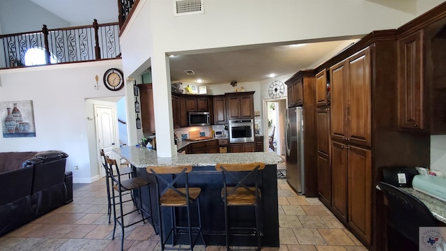 kitchen with appliances with stainless steel finishes, a high ceiling, dark brown cabinetry, a breakfast bar, and kitchen peninsula