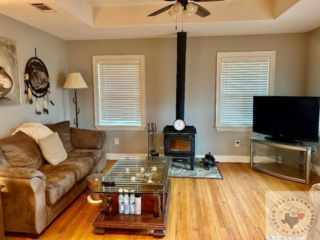 living room with a raised ceiling, a wood stove, hardwood / wood-style floors, and ceiling fan