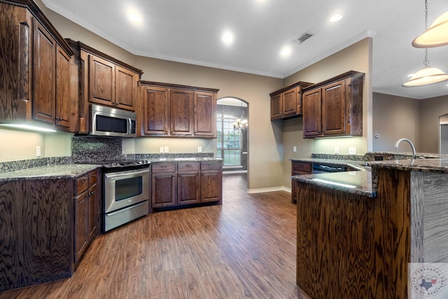 kitchen featuring appliances with stainless steel finishes, dark stone countertops, decorative light fixtures, ornamental molding, and dark hardwood / wood-style flooring