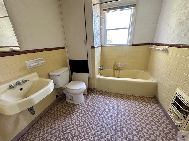 bathroom featuring toilet, tile walls, sink, heating unit, and a tub