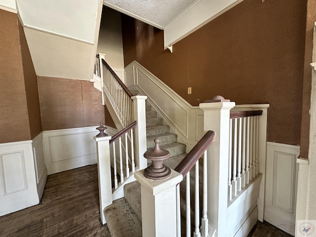 staircase with hardwood / wood-style flooring, ornamental molding, and a textured ceiling