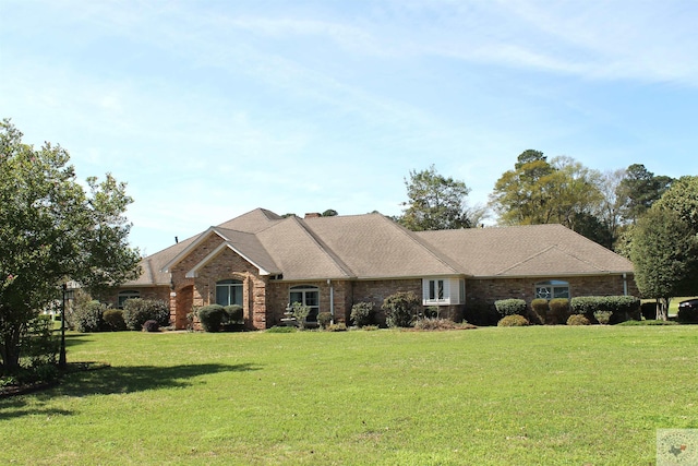 ranch-style house with brick siding, a front lawn, and roof with shingles
