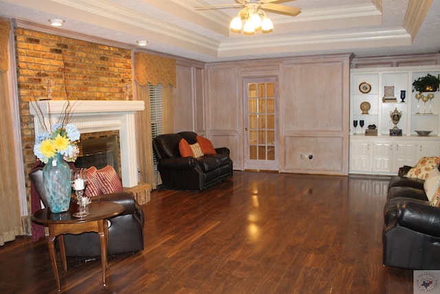 living room featuring dark hardwood / wood-style flooring, a fireplace, ornamental molding, ceiling fan, and a tray ceiling