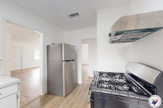 2451 Oaklawn Dr, Texarkana, TX 75501 - kitchen featuring wall chimney range hood, light wood-type flooring, visible vents, white cabinets, and appliances with stainless steel finishes