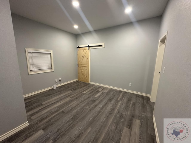 empty room with a barn door and dark hardwood / wood-style flooring