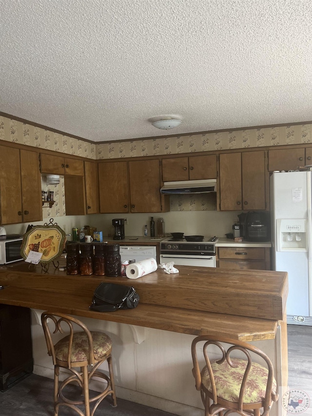 kitchen with white appliances, a kitchen bar, and a textured ceiling