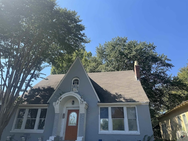 tudor-style house featuring roof with shingles and a chimney