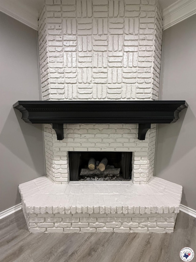 interior details featuring crown molding, wood finished floors, baseboards, and a brick fireplace