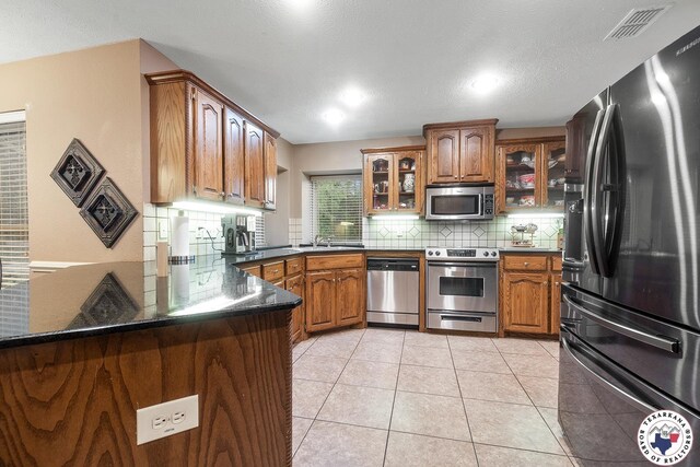 6404 N Park Rd, Texarkana, TX 75503 - kitchen with tasteful backsplash, brown cabinetry, stainless steel appliances, and a peninsula