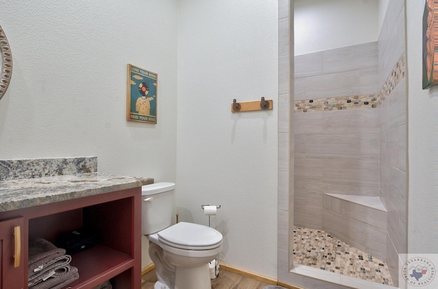 bathroom with a tile shower, wood-type flooring, toilet, and vanity