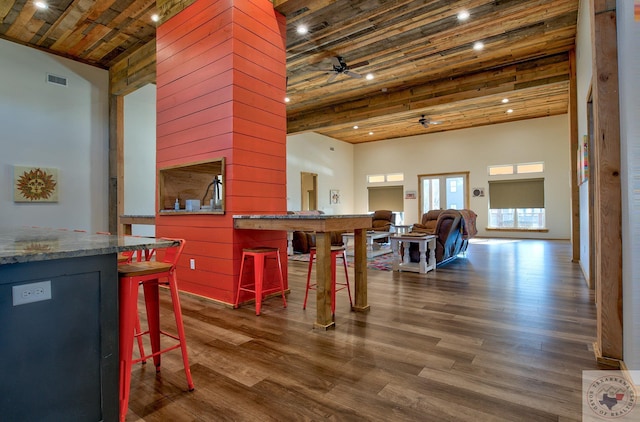 interior space with a high ceiling, dark hardwood / wood-style flooring, ceiling fan, wooden ceiling, and a breakfast bar area