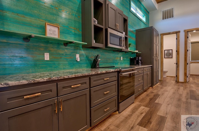 kitchen featuring appliances with stainless steel finishes, dark stone countertops, light hardwood / wood-style floors, backsplash, and gray cabinetry