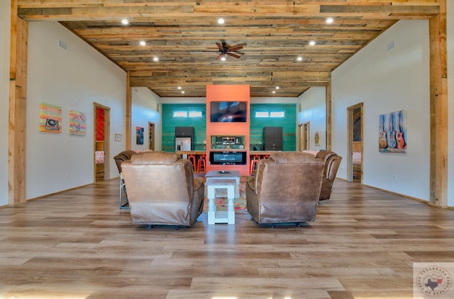 living room with ceiling fan, a high ceiling, light hardwood / wood-style flooring, and wood ceiling