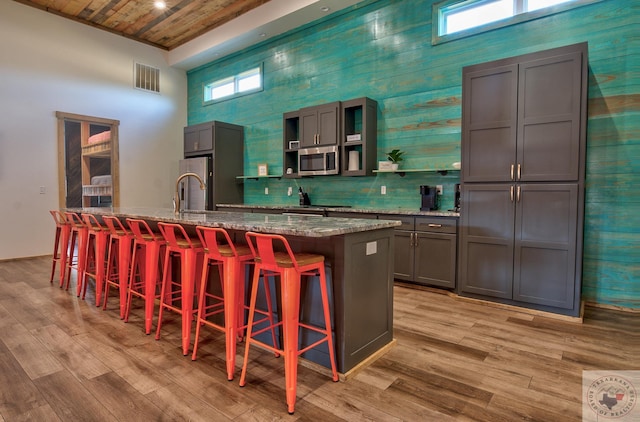 kitchen featuring wood ceiling, stainless steel appliances, a kitchen island with sink, stone counters, and a breakfast bar area