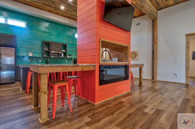 kitchen with a kitchen breakfast bar, kitchen peninsula, appliances with stainless steel finishes, wooden ceiling, and dark hardwood / wood-style floors