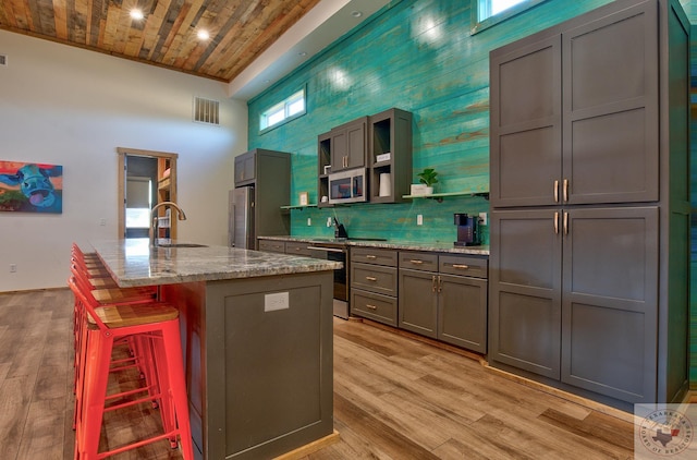 kitchen featuring a kitchen breakfast bar, light stone countertops, wood ceiling, a center island with sink, and stainless steel appliances