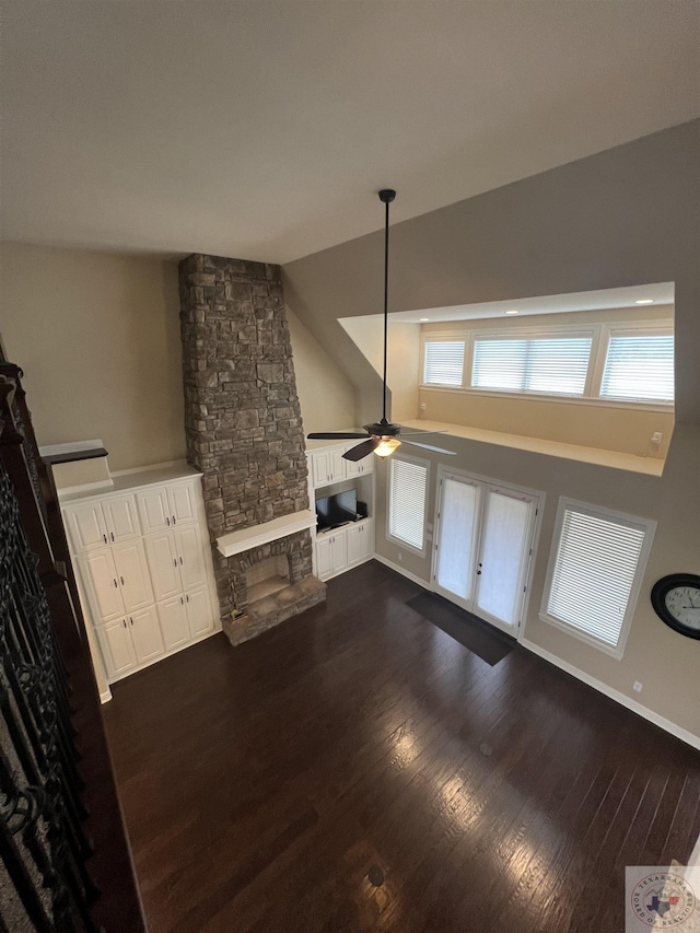 unfurnished living room featuring ceiling fan, vaulted ceiling, a stone fireplace, and dark hardwood / wood-style flooring