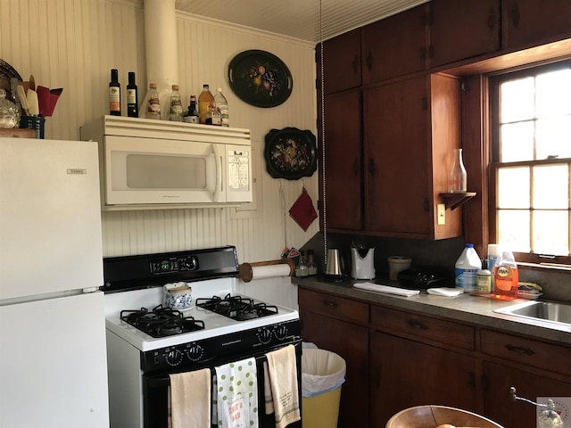 kitchen with sink, dark brown cabinets, white appliances, and wooden walls