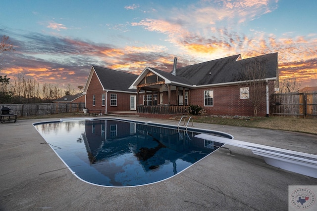 pool at dusk featuring a diving board and a patio