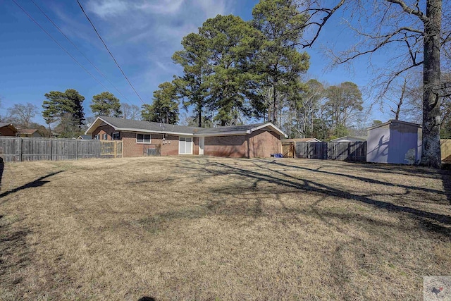 rear view of property featuring an outbuilding, a storage shed, brick siding, fence, and a lawn