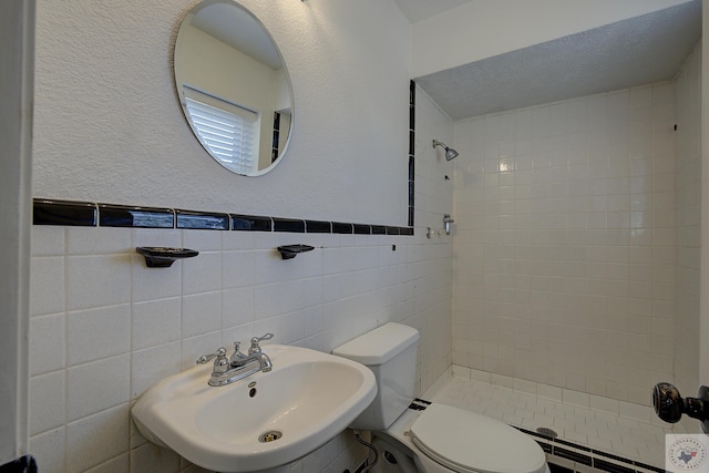 bathroom featuring tile walls, toilet, wainscoting, a sink, and a shower stall