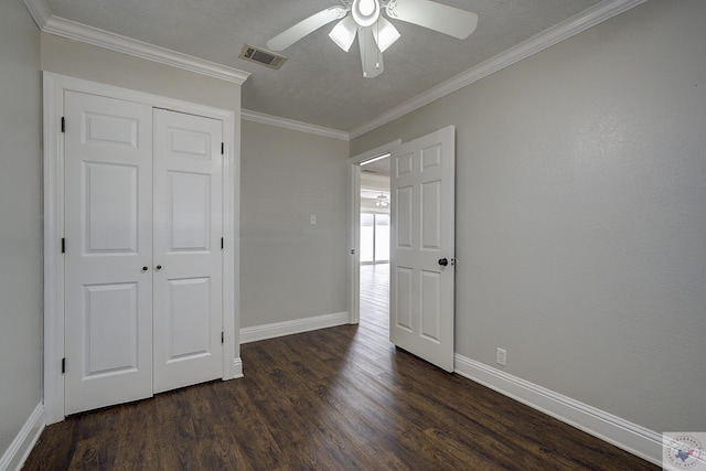 unfurnished bedroom with crown molding, a closet, visible vents, dark wood-type flooring, and baseboards