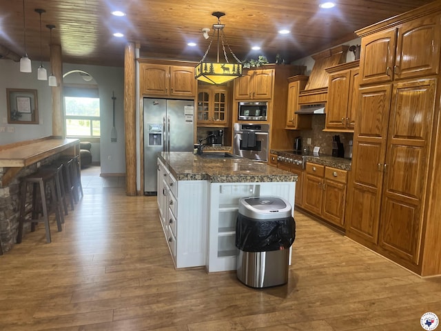 kitchen with a sink, brown cabinetry, light wood-style floors, stainless steel appliances, and under cabinet range hood