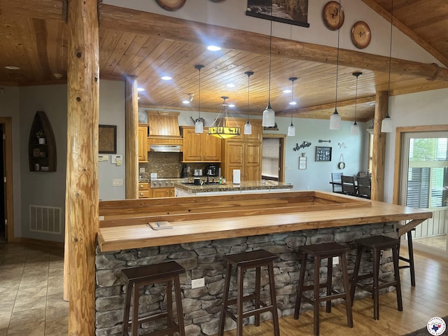 kitchen featuring pendant lighting, a kitchen bar, wooden ceiling, under cabinet range hood, and visible vents