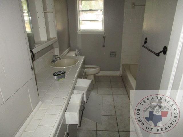 bathroom featuring vanity, toilet, tile patterned floors, and a tub to relax in