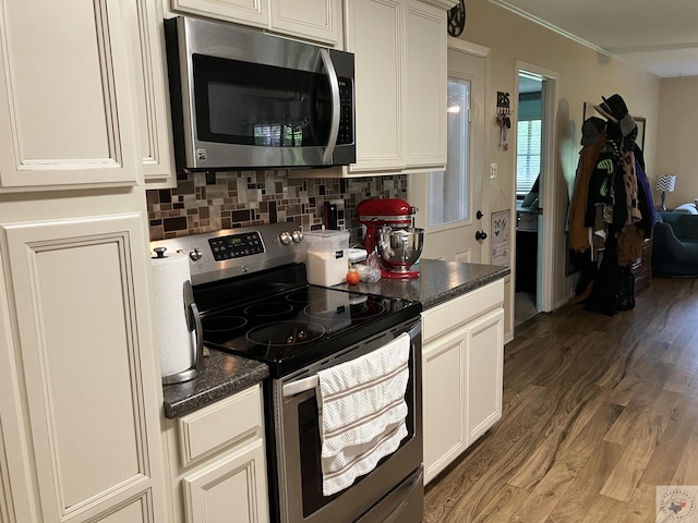 kitchen featuring appliances with stainless steel finishes, backsplash, dark wood-type flooring, white cabinets, and dark stone counters