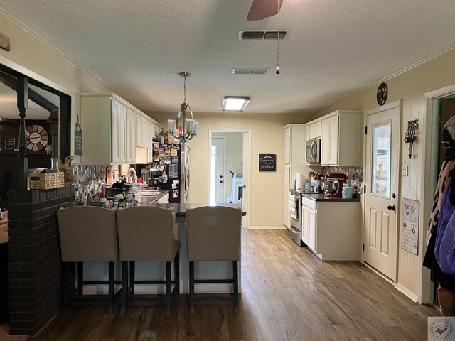 kitchen featuring a kitchen bar, hanging light fixtures, white cabinets, kitchen peninsula, and stainless steel appliances