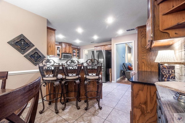 kitchen with appliances with stainless steel finishes, decorative backsplash, a kitchen breakfast bar, kitchen peninsula, and light tile patterned floors