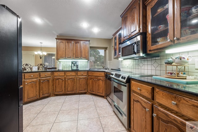 kitchen featuring light tile patterned floors, decorative light fixtures, an inviting chandelier, backsplash, and stainless steel appliances