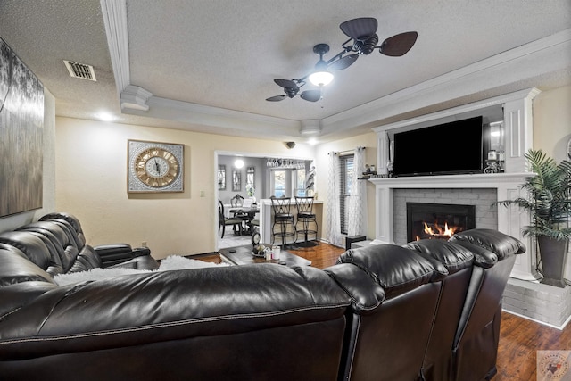 living room with a textured ceiling, dark hardwood / wood-style floors, a raised ceiling, ceiling fan, and a fireplace