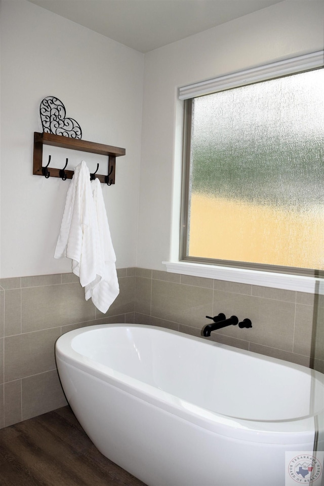 bathroom with hardwood / wood-style floors, a bath, and tile walls