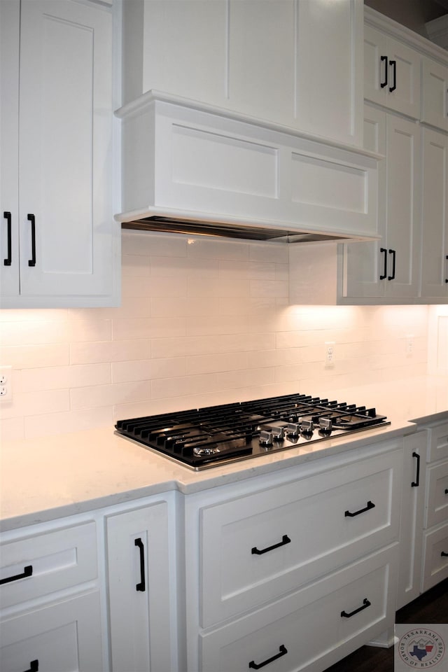 kitchen with white cabinetry, premium range hood, backsplash, light stone counters, and stainless steel gas stovetop