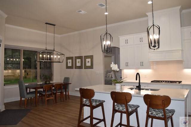 kitchen featuring white cabinetry, dark hardwood / wood-style flooring, sink, ornamental molding, and a center island with sink