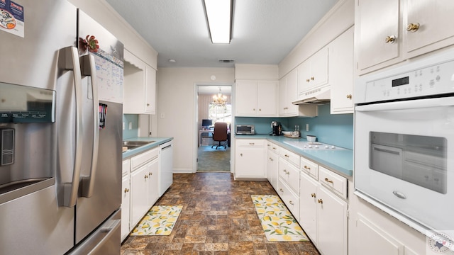 kitchen featuring stone finish floor, under cabinet range hood, a sink, white cabinetry, and white appliances