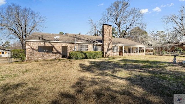 rear view of house featuring a yard, brick siding, and a chimney