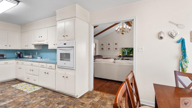 kitchen with stone finish floor, under cabinet range hood, white cabinetry, white appliances, and an inviting chandelier