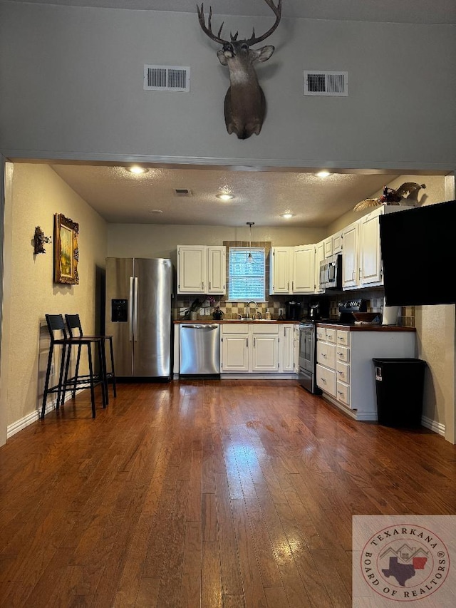 kitchen featuring dark hardwood / wood-style flooring, white cabinetry, stainless steel appliances, and decorative backsplash